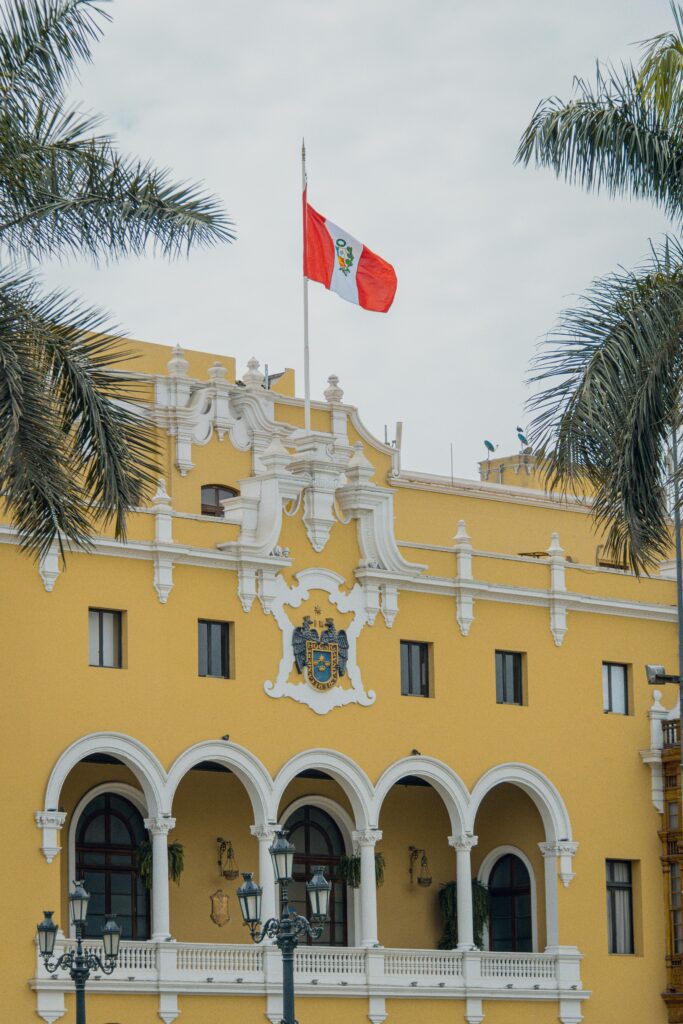 The ornate yellow facade of Lima's Municipal Palace with Peru's flag atop.