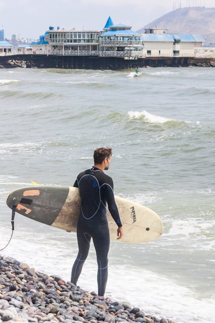 Surfer in wetsuit holding surfboard on rocky Lima beach by the ocean. Perfect for coastal and adventure themes.
