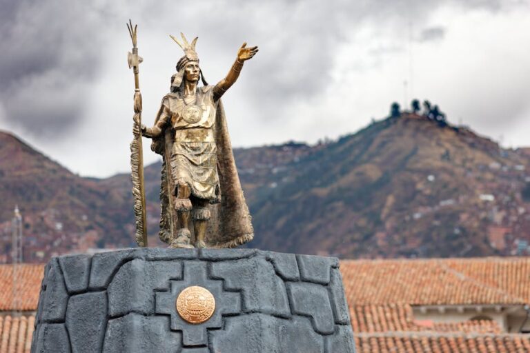 A majestic Inca statue stands prominently in Cusco, Peru with the Andes mountain range in the background.