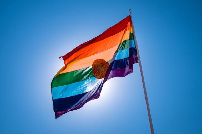 Vibrant rainbow flag of Cusco waving against a clear blue sky.