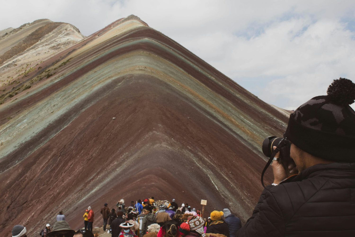 Photographer capturing the vibrant Rainbow Mountain in Peru with a crowd of tourists.