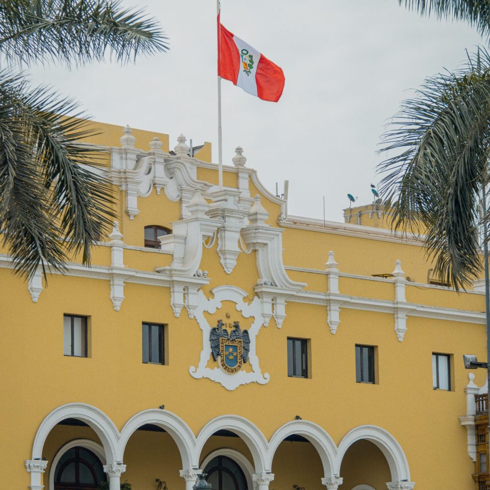 The ornate yellow facade of Lima's Municipal Palace with Peru's flag atop.