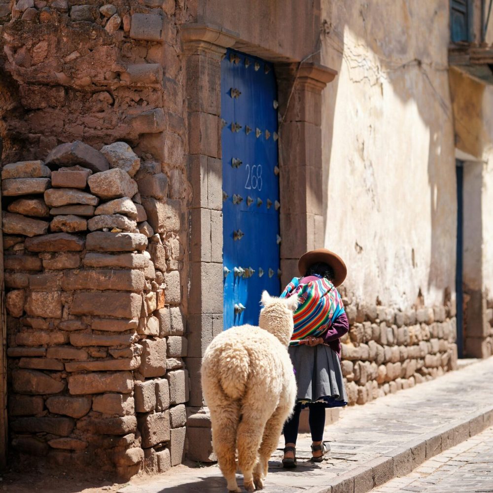 A woman dressed in traditional attire walks with an alpaca in a rustic village street in Cusco, Peru.